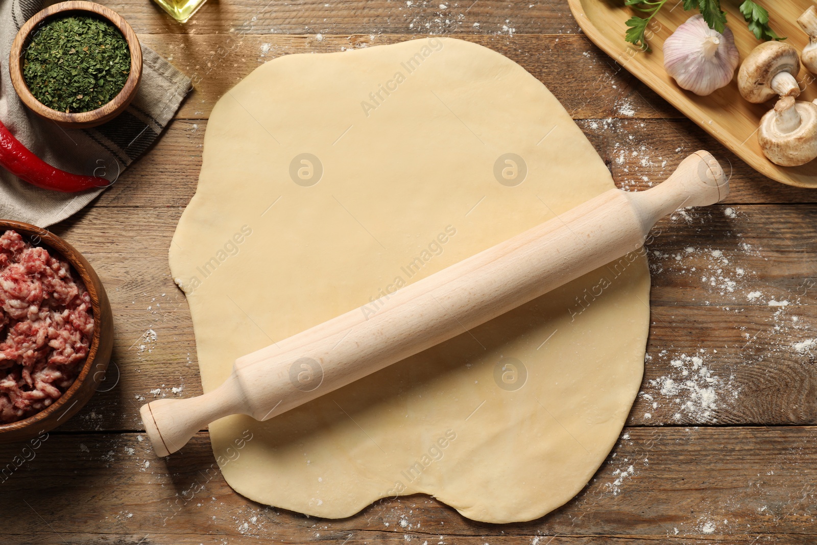 Photo of Raw dough, rolling pin and products on wooden table, flat lay