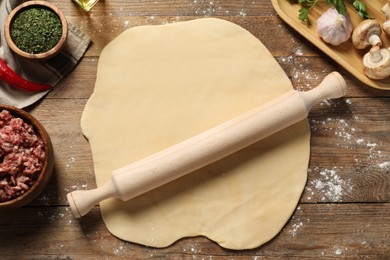 Raw dough, rolling pin and products on wooden table, flat lay