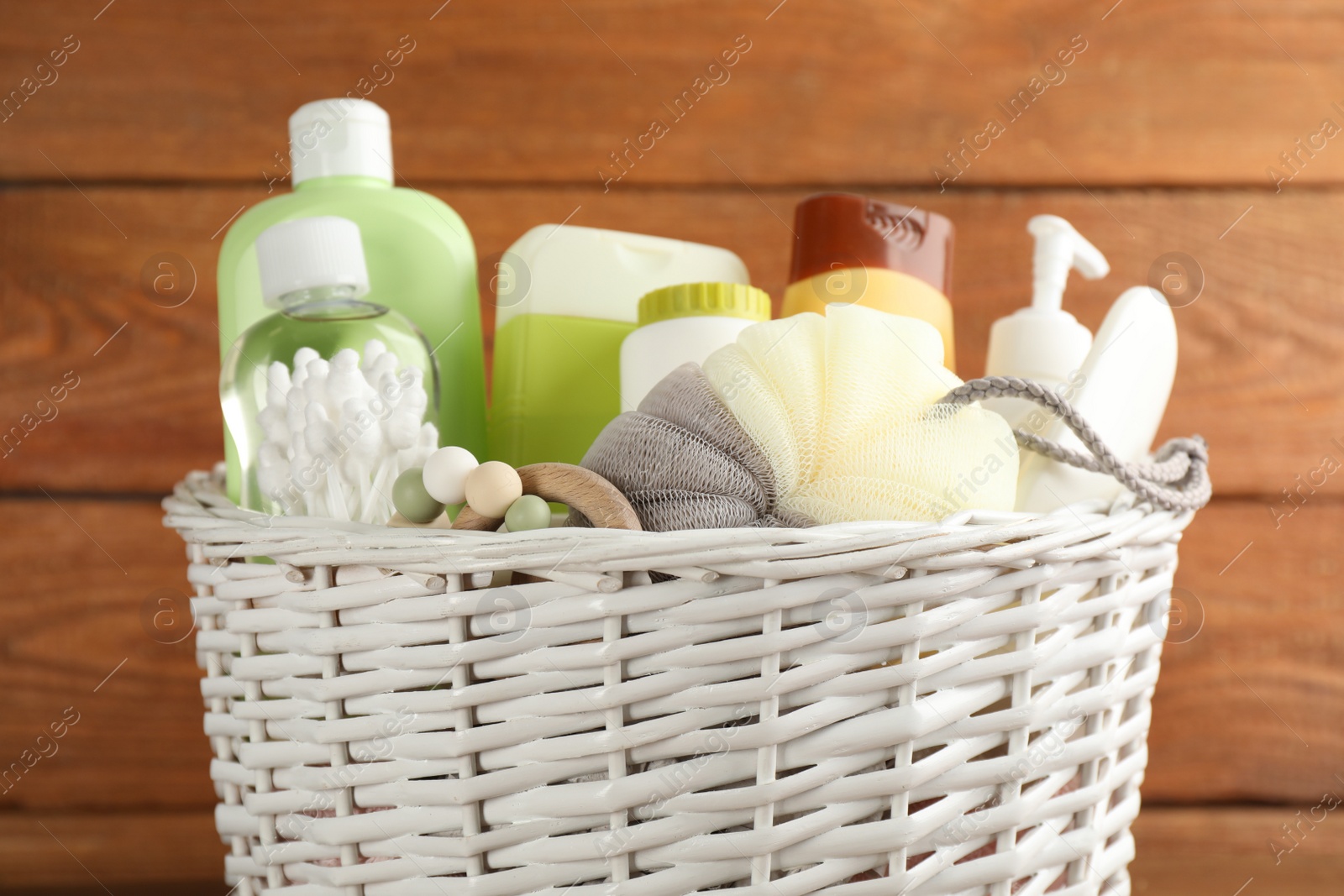 Photo of Wicker basket full of different baby cosmetic products, accessories and toy on wooden background, closeup