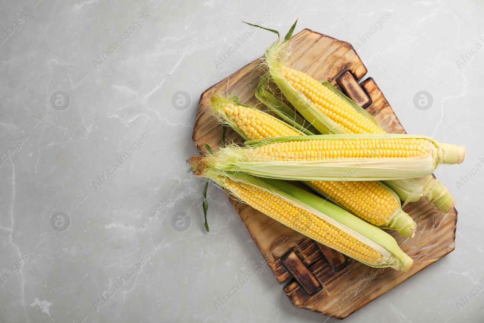 Photo of Tasty sweet corn cobs on wooden board, top view