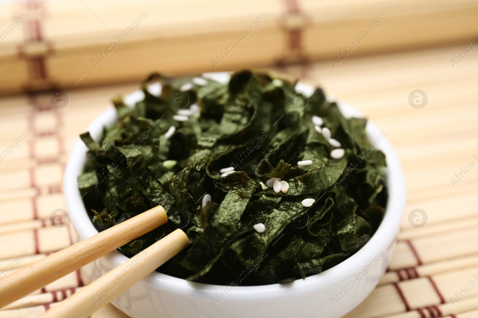 Photo of Chopped nori sheets with sesame and chopsticks on bamboo mat, closeup