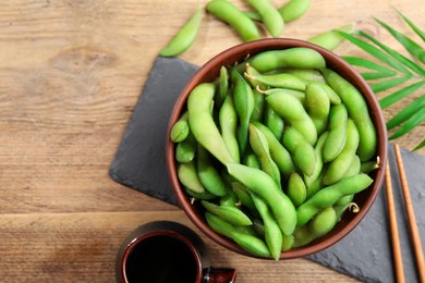 Photo of Green edamame beans in pods served with soy sauce on wooden table, flat lay