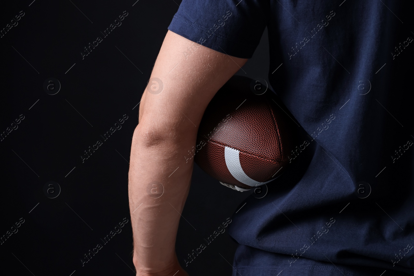 Photo of Athletic man with American football ball on black background, closeup
