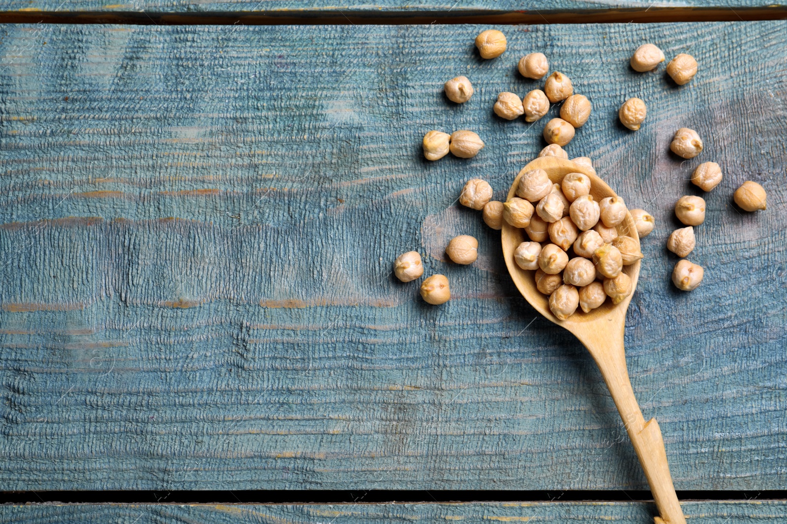 Photo of Raw chickpeas with spoon on blue wooden table, flat lay. Space for text