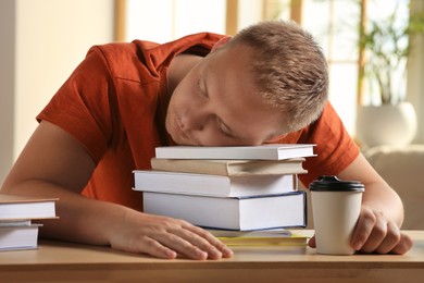 Photo of Tired man sleeping near books at wooden table indoors
