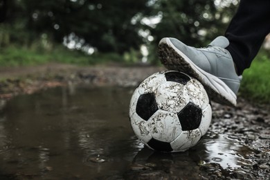 Photo of Man with dirty soccer ball in puddle outdoors, closeup. Space for text