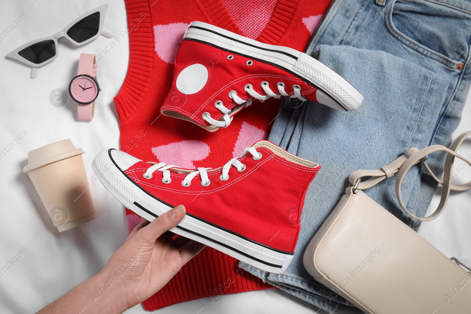 Photo of Woman with new stylish red sneakers, accessories, cup of drink and clothes on white fabric, top view. Casual outfit