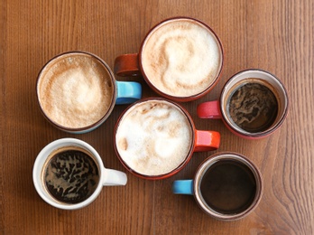 Photo of Cups of fresh aromatic coffee on wooden table, top view