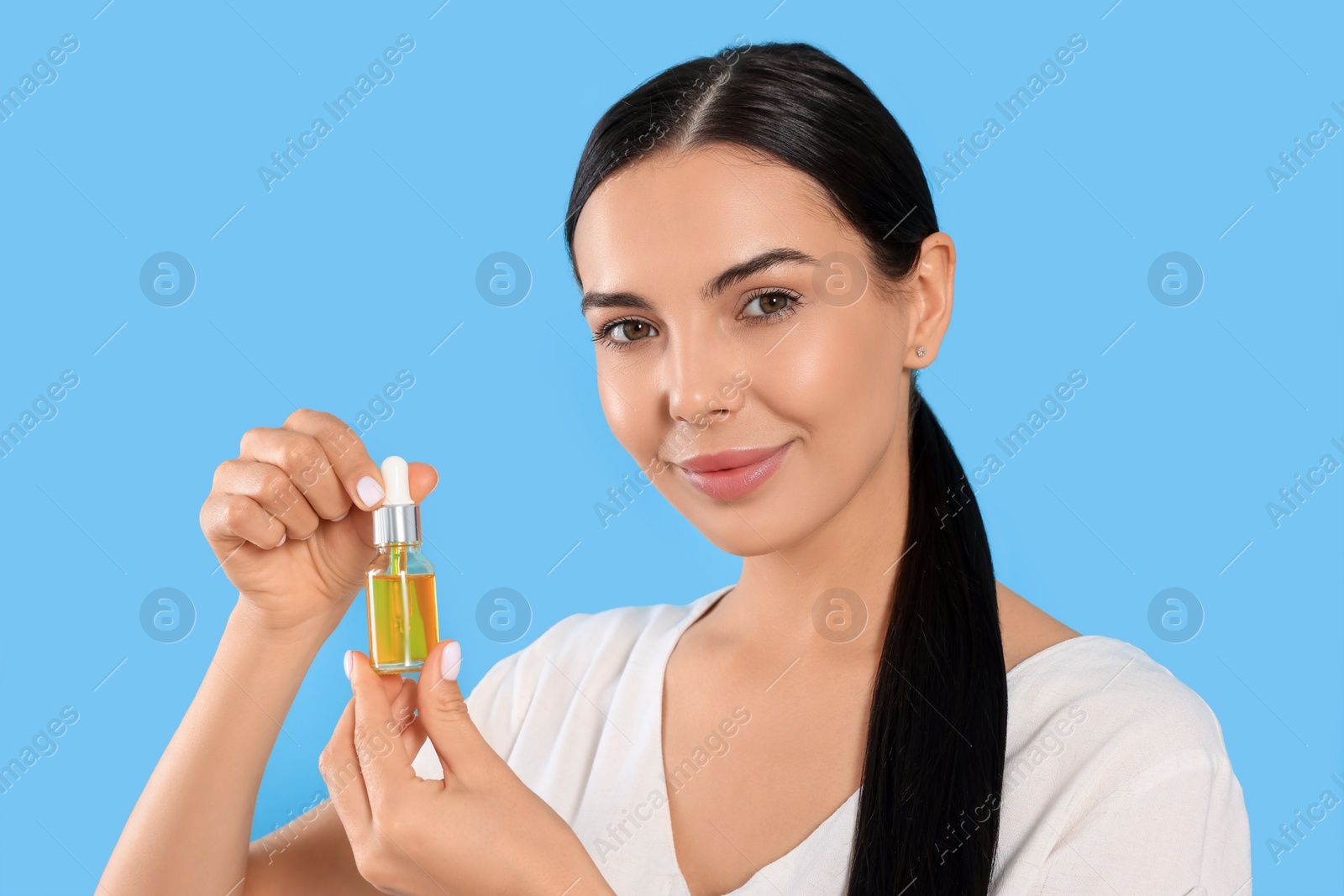 Photo of Young woman with bottle of essential oil on light blue background