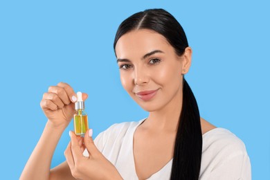 Photo of Young woman with bottle of essential oil on light blue background