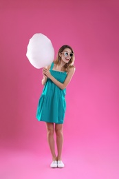 Happy young woman with cotton candy on pink background