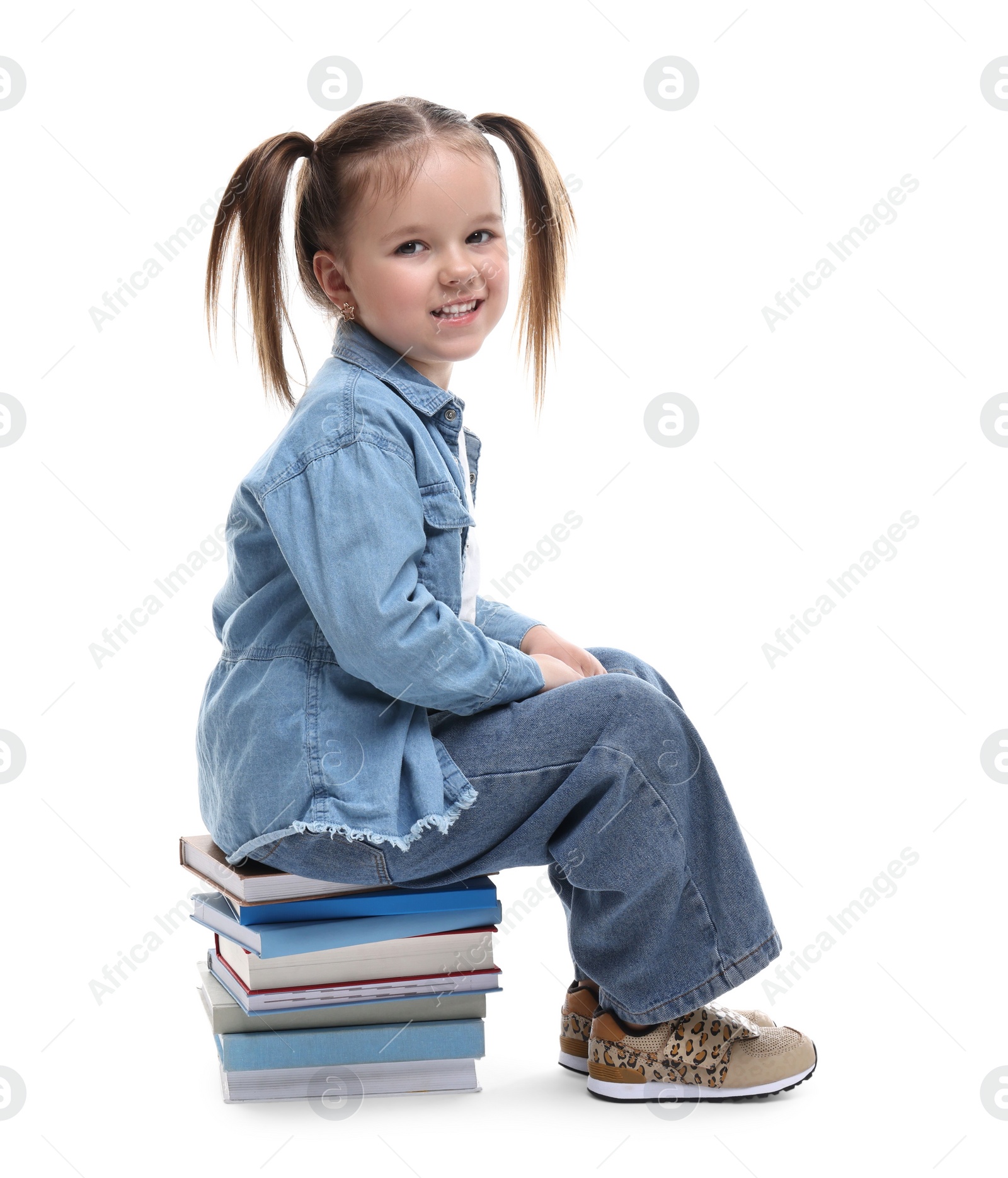 Photo of Cute little girl sitting on stack of books against white background