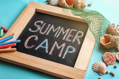 Text "SUMMER CAMP" on small blackboard, colorful chalk and shells