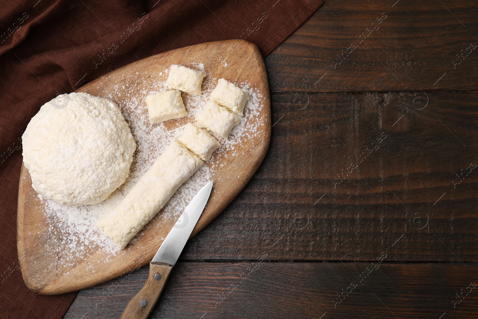 Photo of Making lazy dumplings. Board with raw dough, flour and knife on wooden table, flat lay. Space for text