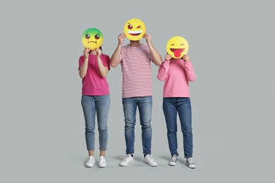 People covering faces with emoticons on grey background