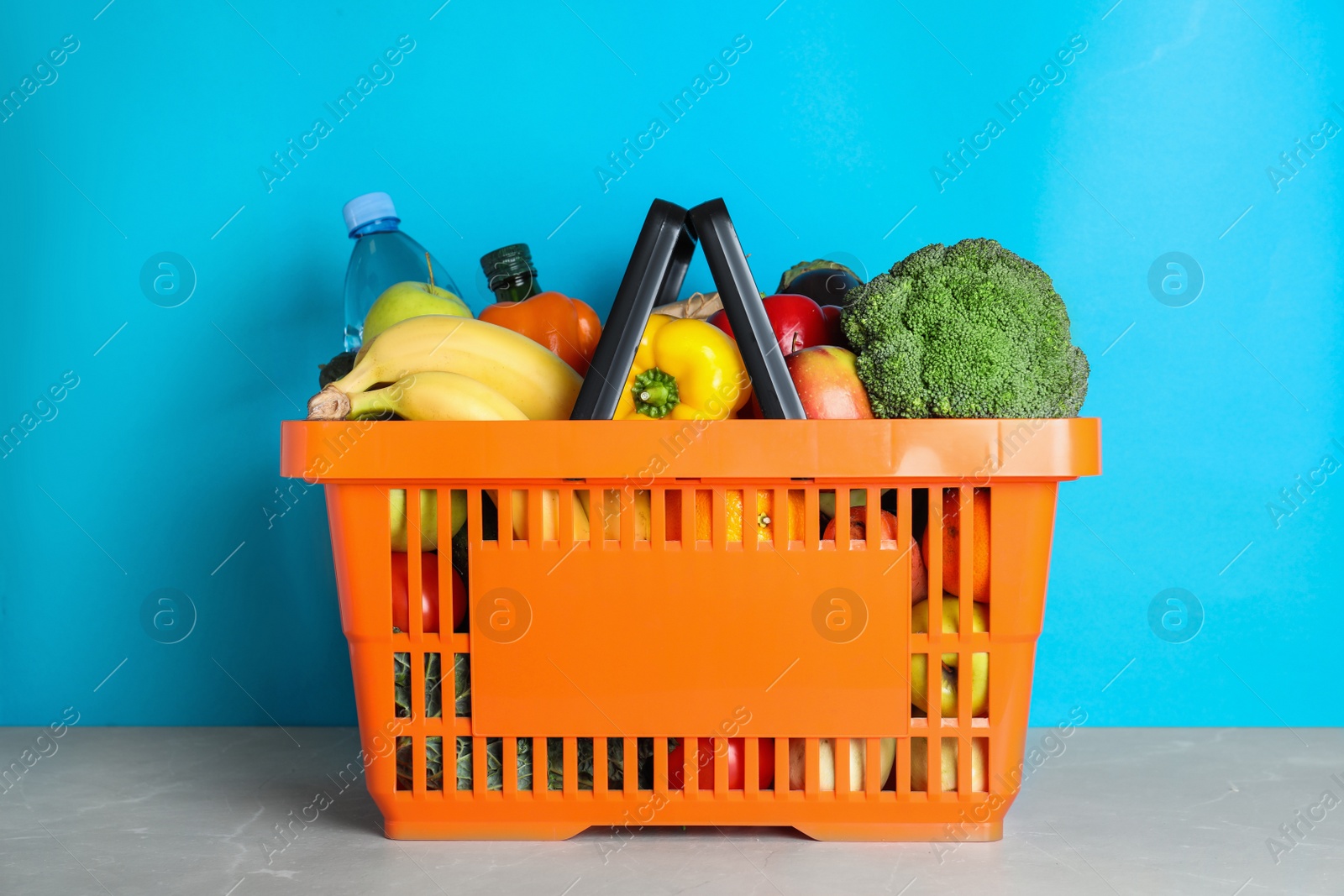 Photo of Shopping basket with grocery products on grey table against light blue background