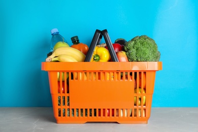 Shopping basket with grocery products on grey table against light blue background