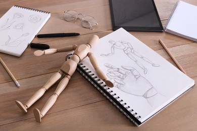 Sketchbook with beautiful drawing, mannequin and pencils on wooden table