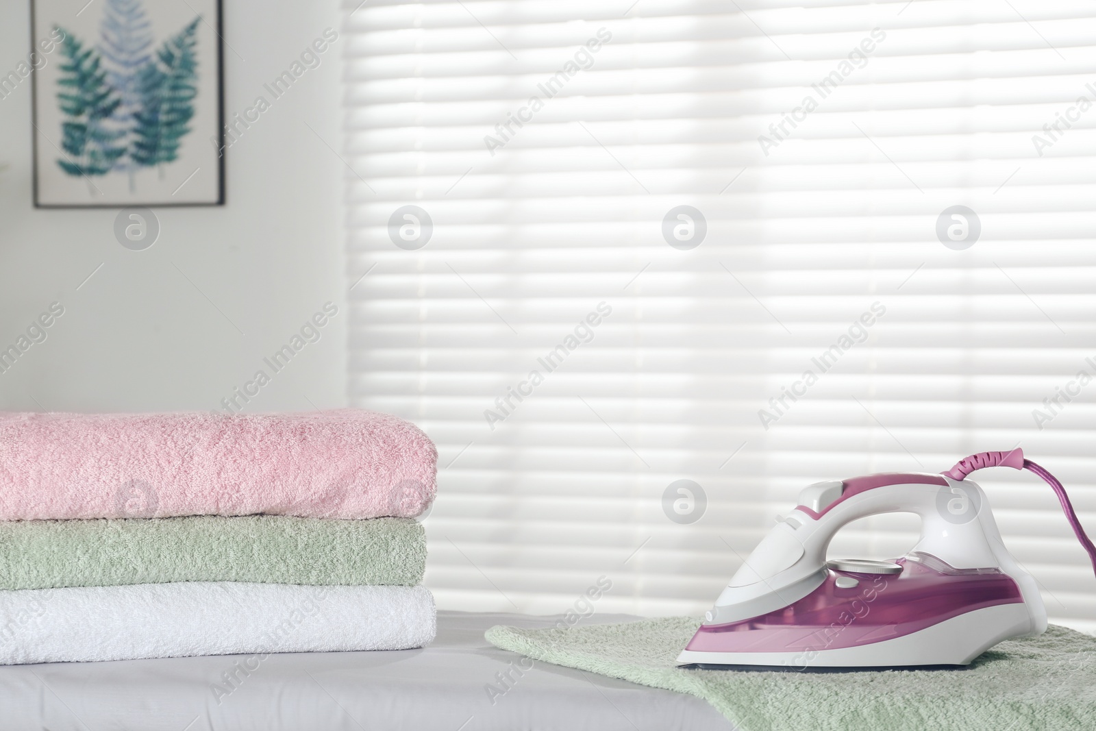 Photo of Modern iron and clean towels on board indoors. Space fot text