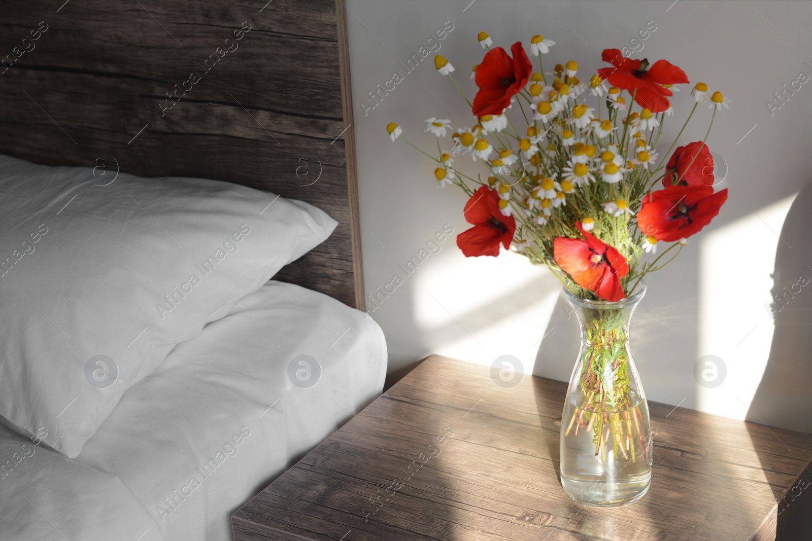 Photo of Glass vase with bouquet of beautiful wildflowers on nightstand in bedroom