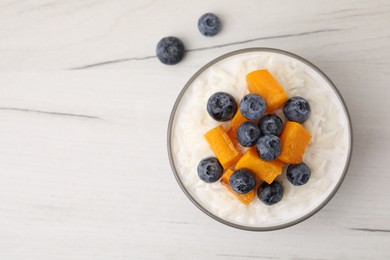 Photo of Bowl of delicious rice porridge with blueberries and pumpkin on white table, top view. Space for text