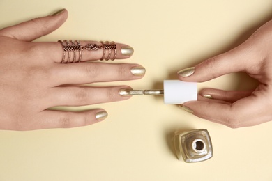 Woman applying nail polish on color background, top view