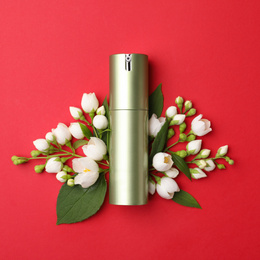 Bottle of cosmetic product and flowers on red background, flat lay