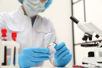 Photo of Scientist examining pill with magnifying glass in laboratory, closeup