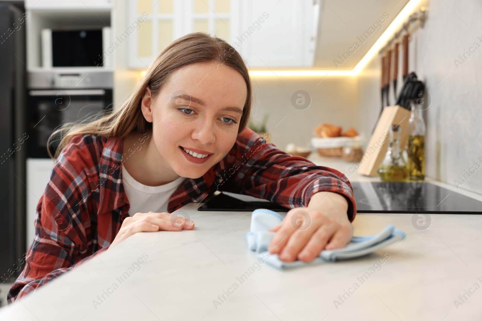 Photo of Woman with microfiber cloth cleaning white marble countertop in kitchen