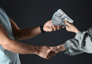 Photo of Woman shaking hands with man and offering bribe on black background, closeup