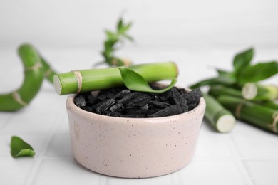 Photo of Fresh bamboo and charcoal on white tiled table, closeup