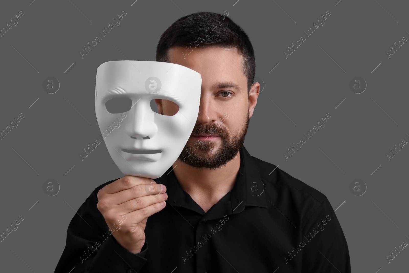 Photo of Multiple personality concept. Man covering face with mask on grey background