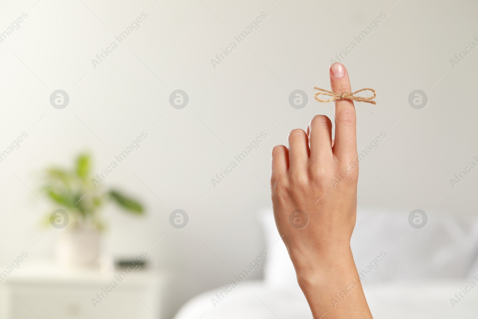 Photo of Woman showing index finger with tied bow as reminder indoors, closeup. Space for text