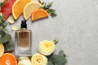 Flat lay composition with bottle of perfume and fresh citrus fruits on light grey table. space for text
