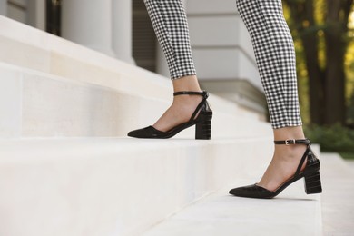 Photo of Woman in stylish black shoes walking up stairs, closeup