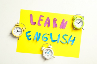 Note with phrase Learn English and alarm clocks on white background, flat lay