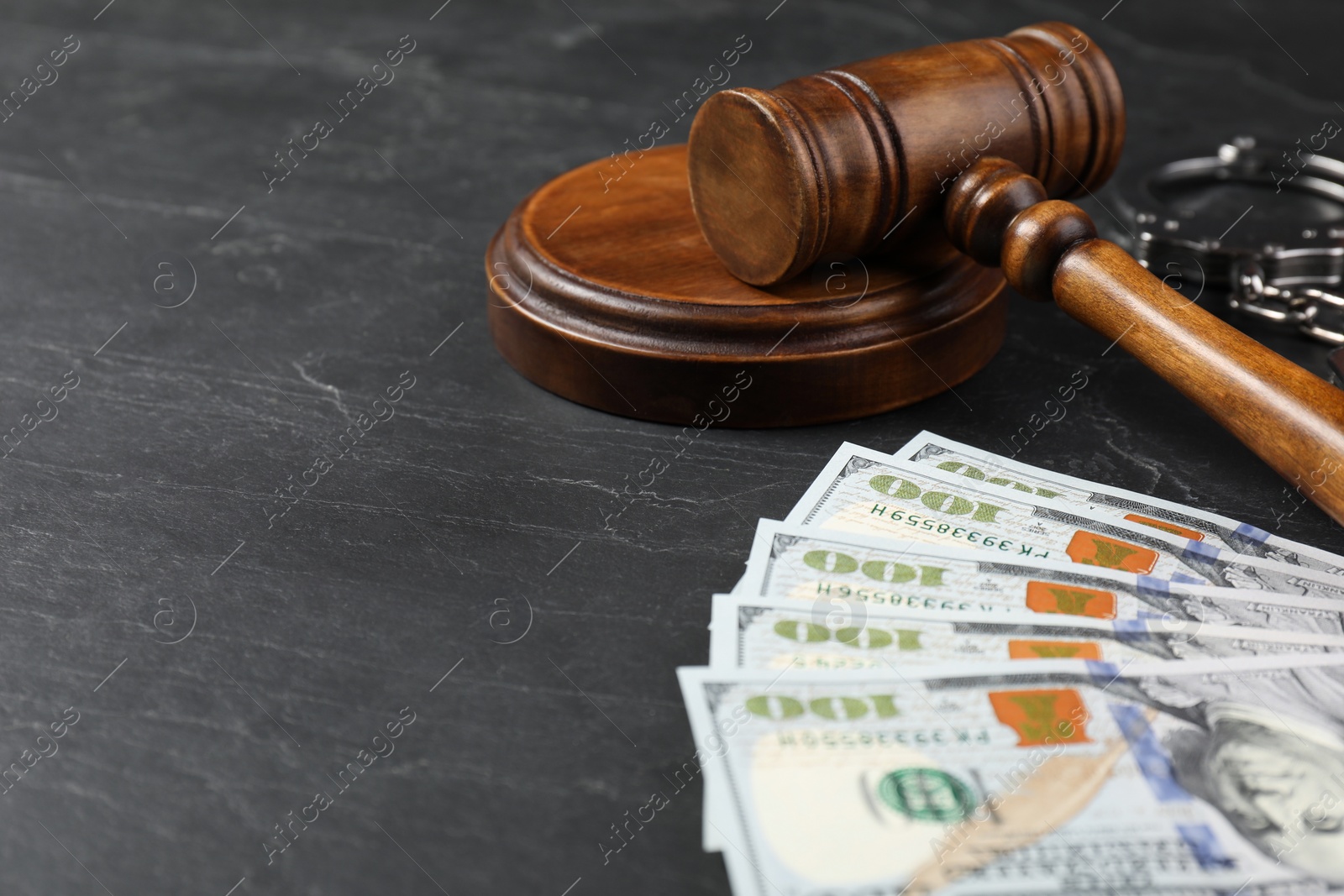 Photo of Judge's gavel, money and handcuffs on dark grey table. Space for text