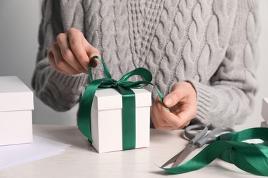 Woman decorating gift box at white table, closeup. Christmas present