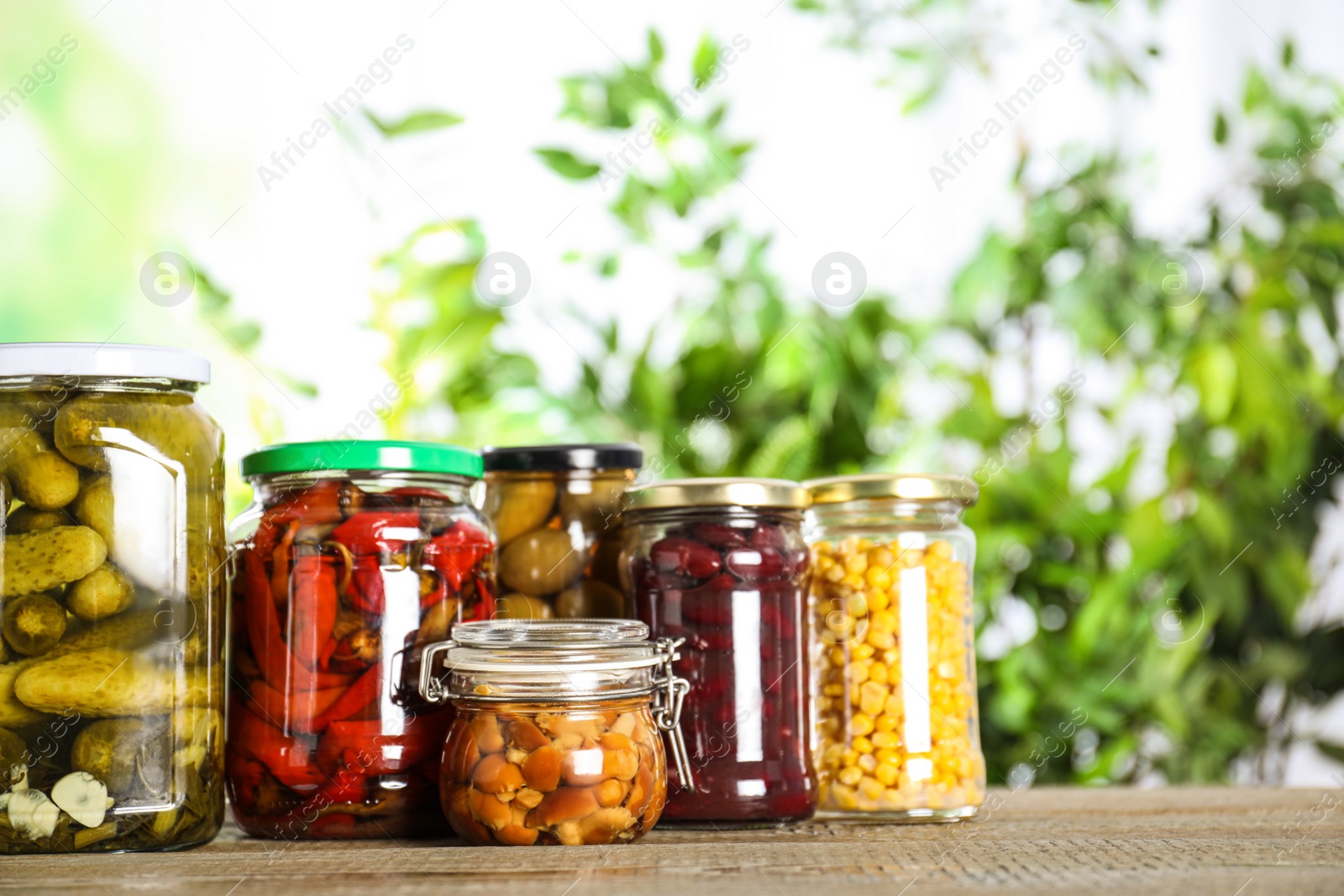 Photo of Glass jars of different pickled vegetables on wooden table