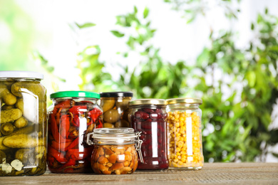 Glass jars of different pickled vegetables on wooden table