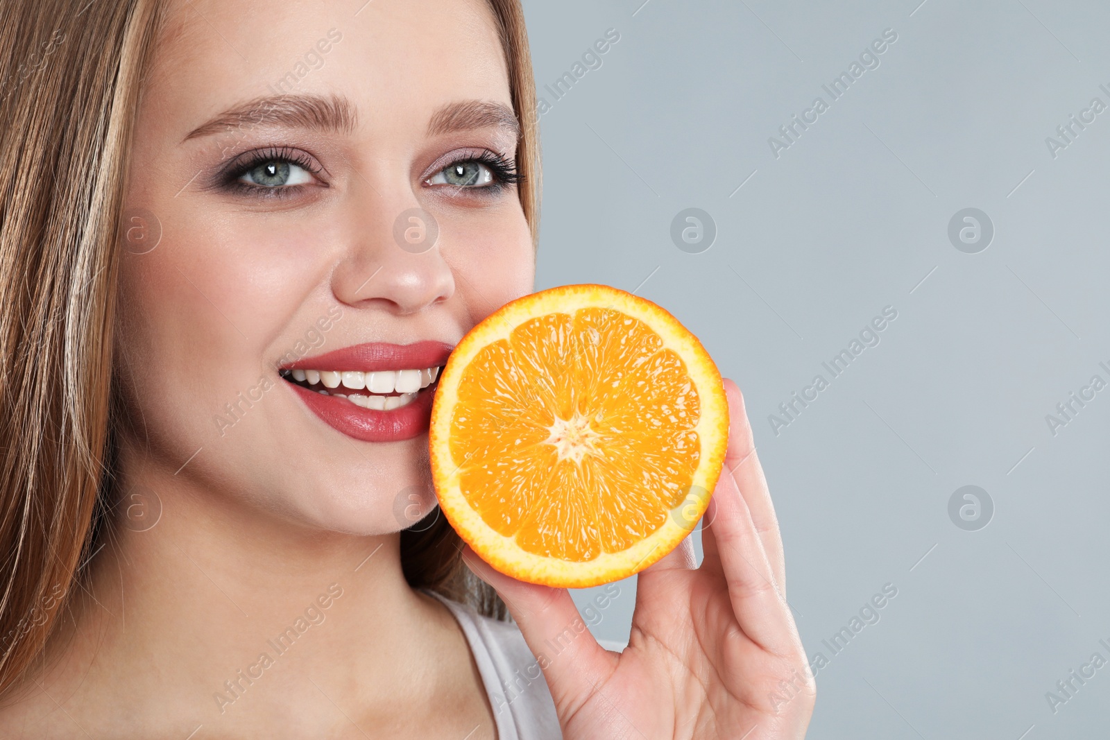 Photo of Young woman with cut orange on grey background. Vitamin rich food