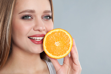 Photo of Young woman with cut orange on grey background. Vitamin rich food