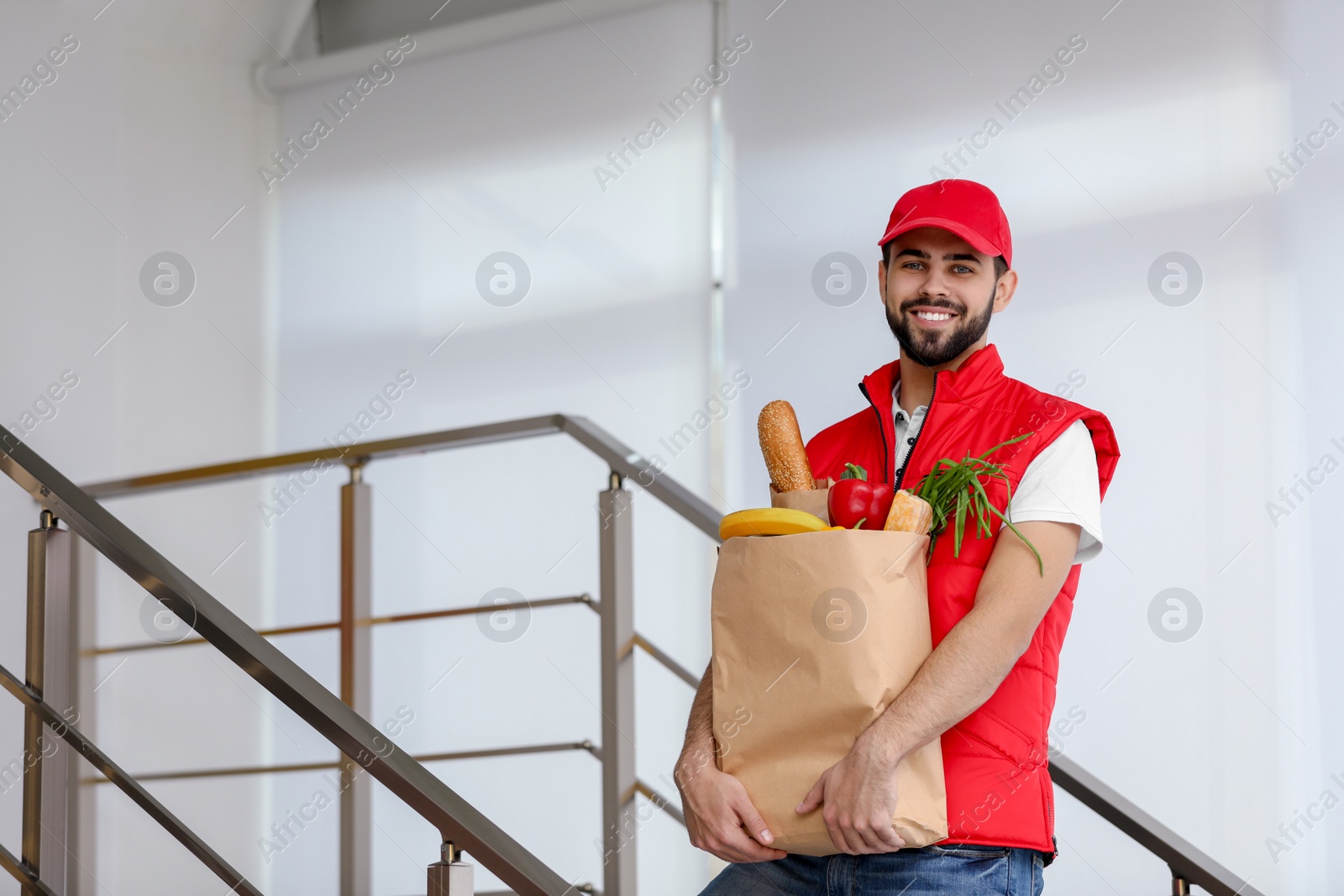 Photo of Man holding paper bag with fresh products on staircase, space for text. Food delivery service