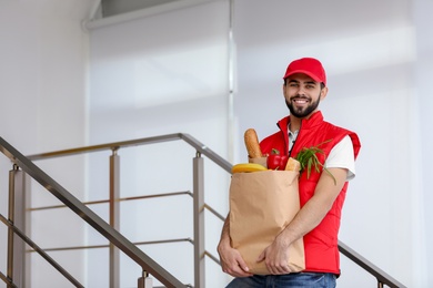 Photo of Man holding paper bag with fresh products on staircase, space for text. Food delivery service