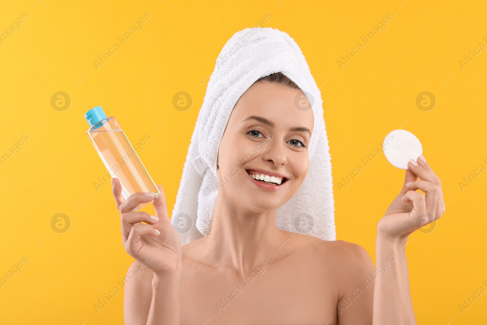 Photo of Removing makeup. Smiling woman with cotton pad and bottle on yellow background