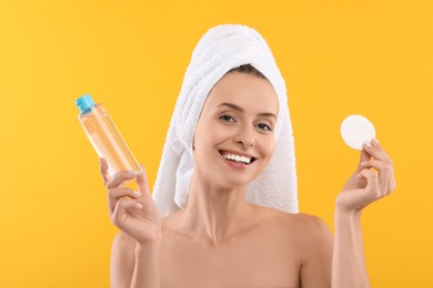 Removing makeup. Smiling woman with cotton pad and bottle on yellow background