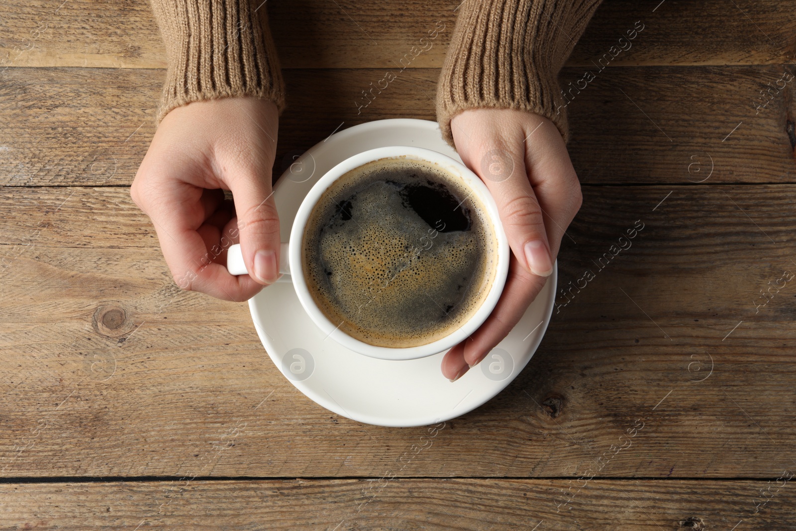 Photo of Woman with cup of hot aromatic coffee at wooden table, top view