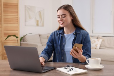 Photo of Happy woman with smartphone and laptop at wooden table in room