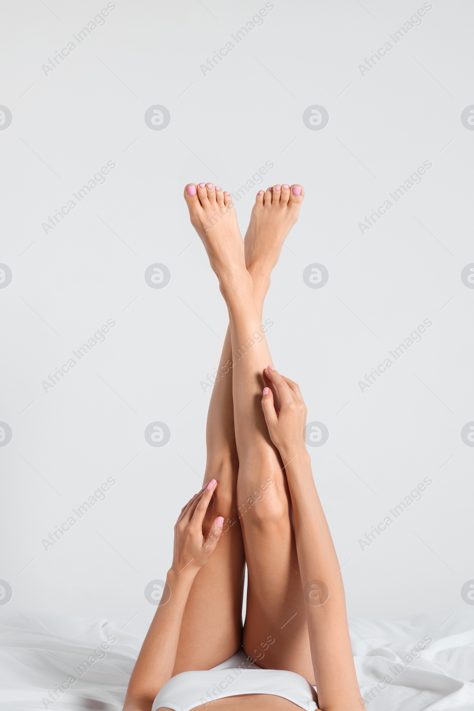 Photo of Woman with beautiful smooth legs on bed against white background, closeup