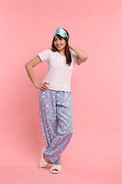 Happy woman in pyjama and sleep mask on pink background